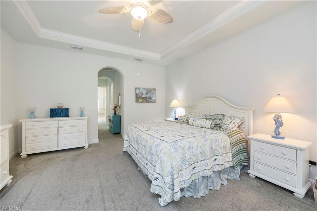 Bedroom with arched walkways, light carpet, a ceiling fan, a raised ceiling, and crown molding