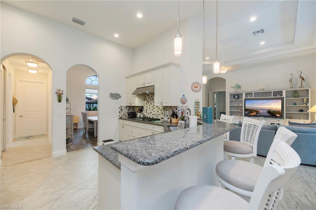 Kitchen featuring arched walkways, dark stone counters, open floor plan, decorative light fixtures, and decorative backsplash