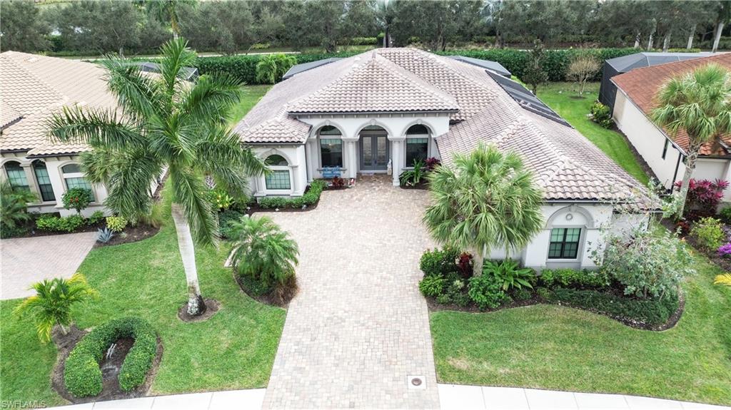 Mediterranean / spanish house with a tiled roof, stucco siding, a front lawn, decorative driveway, and view of wooded area