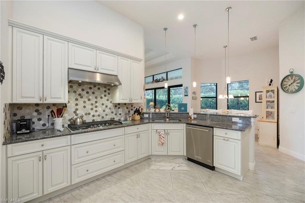 Kitchen featuring dark stone counters, hanging light fixtures, appliances with stainless steel finishes, under cabinet range hood, and tasteful backsplash