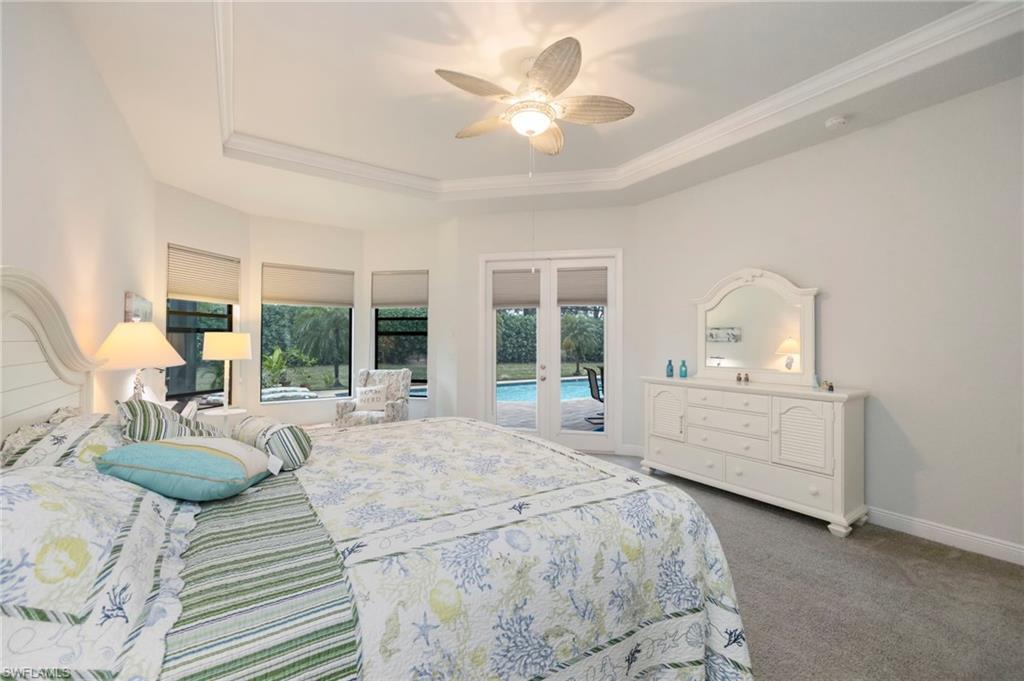 Carpeted bedroom with ceiling fan, ornamental molding, a raised ceiling, and access to exterior