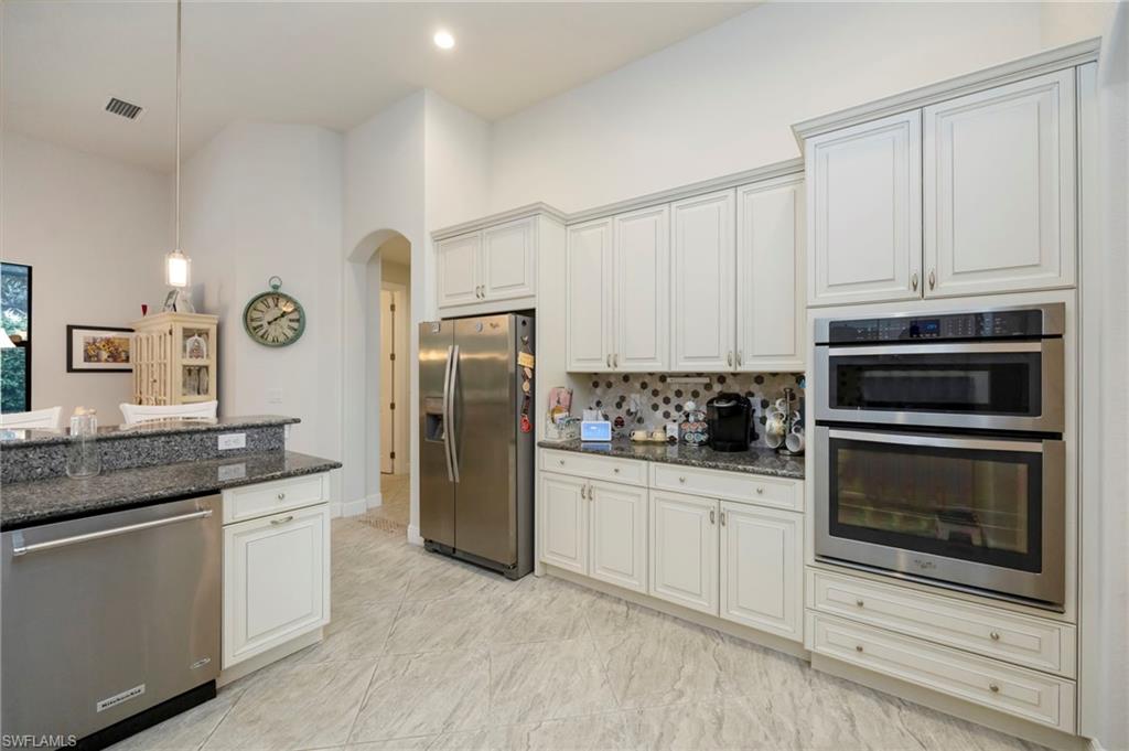 Kitchen with appliances with stainless steel finishes, arched walkways, dark stone countertops, hanging light fixtures, and white cabinets