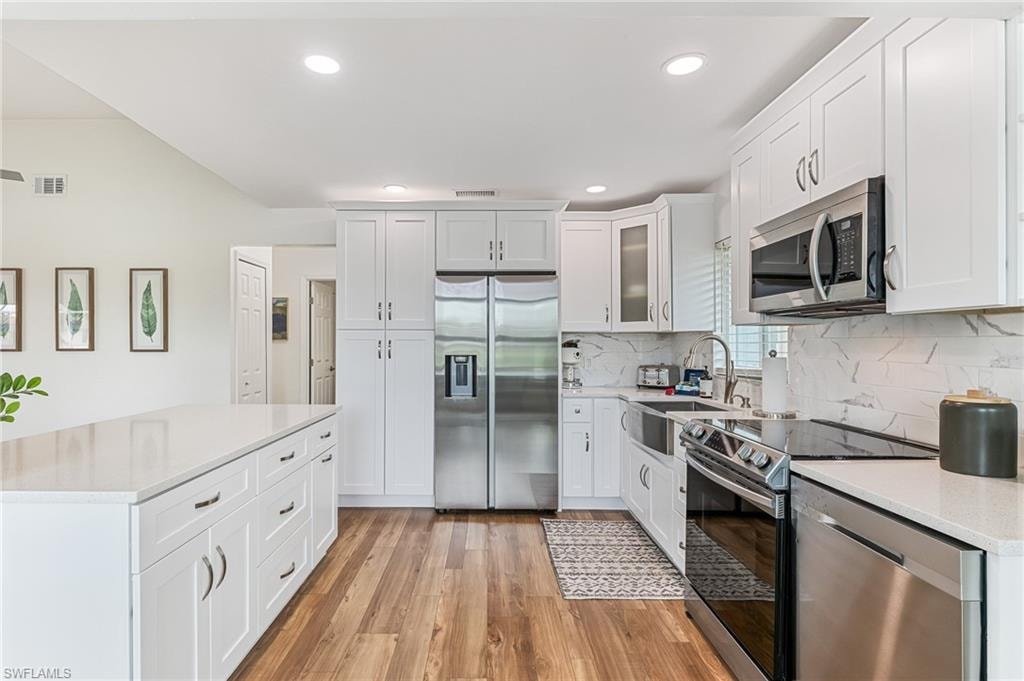 Kitchen with appliances with stainless steel finishes, light wood-style flooring, tasteful backsplash, light countertops, and white cabinets