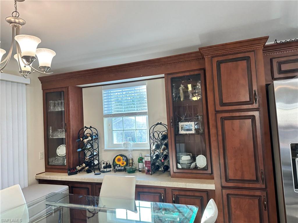 Kitchen with glass insert cabinets, stainless steel fridge, hanging light fixtures, a chandelier, and dark brown cabinets