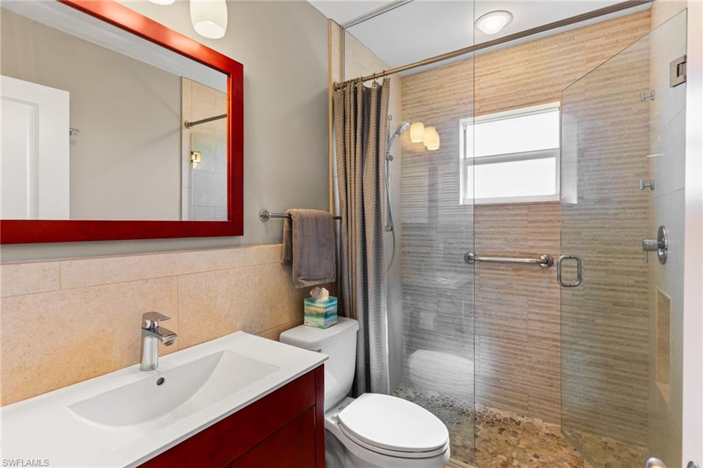 Full bathroom with vanity, a shower stall, tile walls, and a wainscoted wall