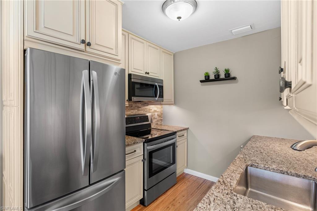 Kitchen with stainless steel appliances, cream cabinetry, dark stone countertops, light wood-style flooring, and backsplash