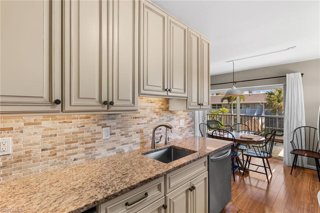 Kitchen featuring cream cabinets, light stone countertops, stainless steel dishwasher, and light wood-type flooring