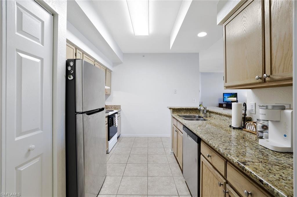 Kitchen with appliances with stainless steel finishes, light stone countertops, a peninsula, light tile patterned floors, and light brown cabinetry
