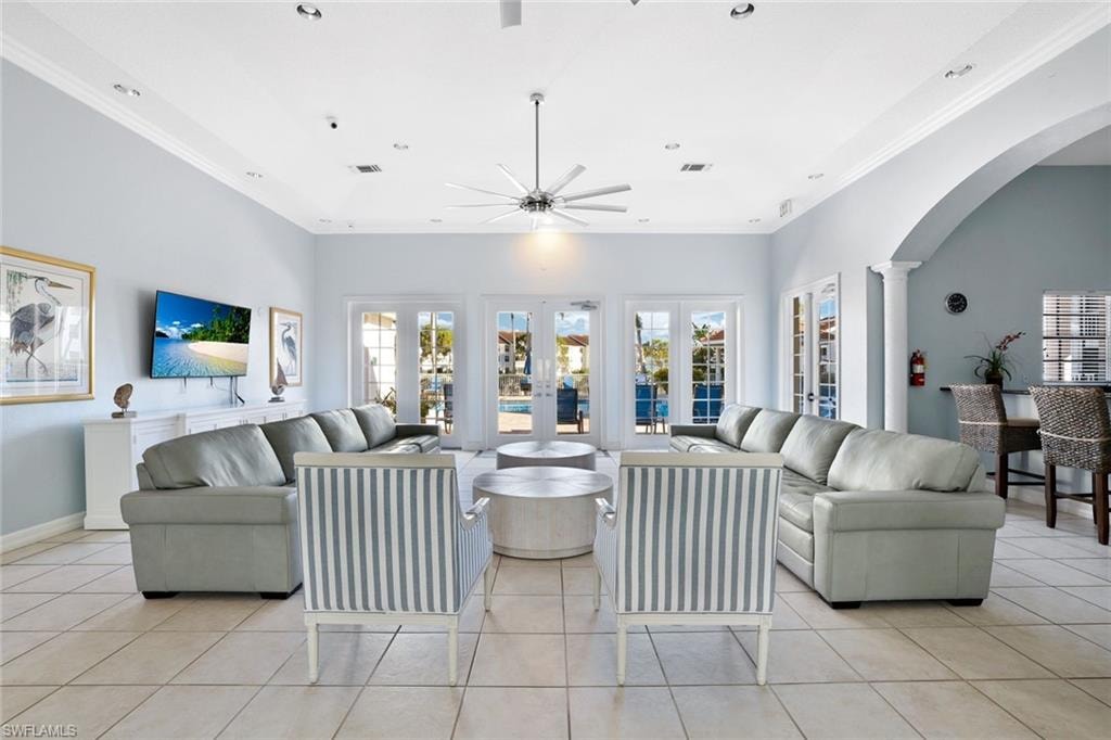 Living room with arched walkways, ornamental molding, light tile patterned floors, ceiling fan, and french doors