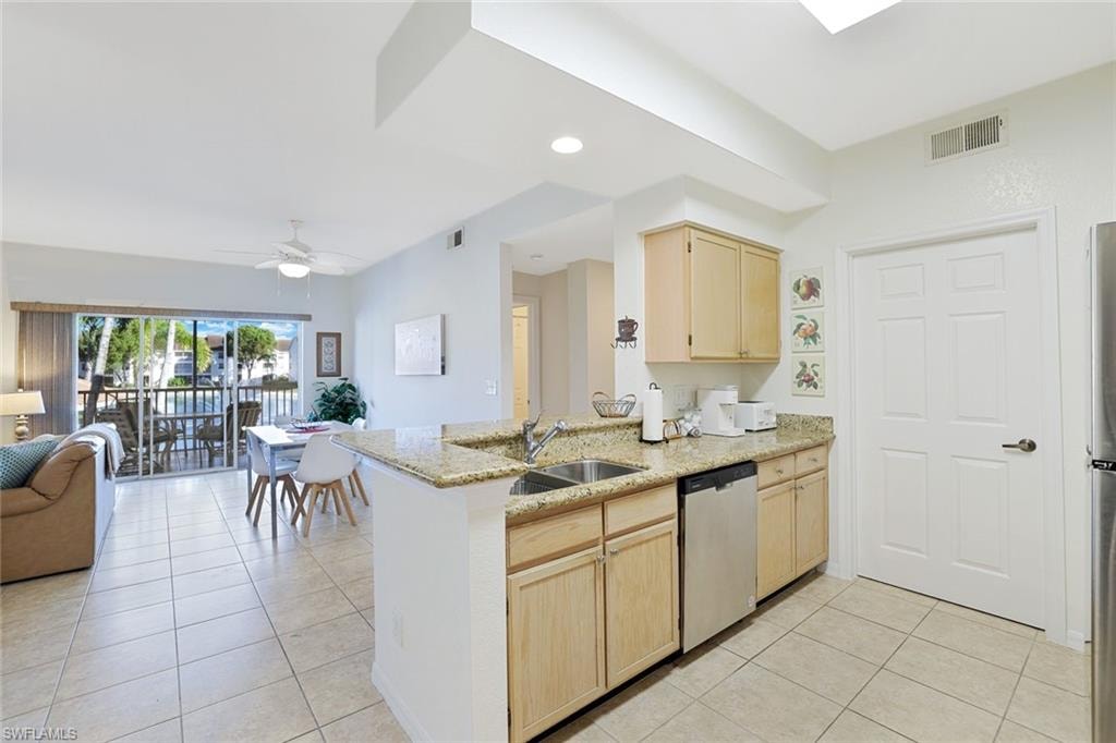 Kitchen with light brown cabinets, open floor plan, light tile patterned floors, light stone countertops, and stainless steel appliances