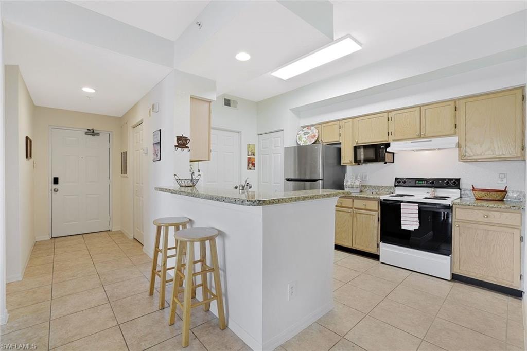 Kitchen featuring light brown cabinetry, a kitchen bar, range with electric stovetop, a peninsula, and recessed lighting
