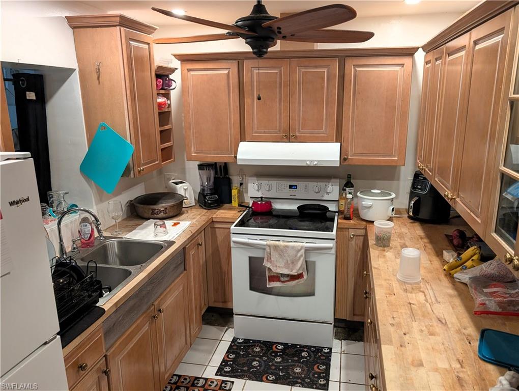 Kitchen with white appliances, under cabinet range hood, ceiling fan, brown cabinets, and light tile patterned floors