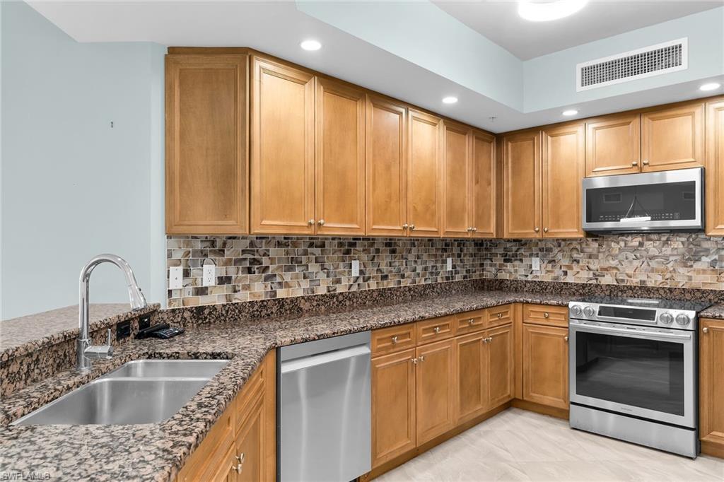 Kitchen featuring dark stone countertops, appliances with stainless steel finishes, brown cabinets, backsplash, and recessed lighting