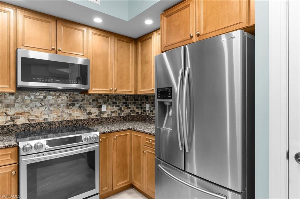 Kitchen featuring appliances with stainless steel finishes, tasteful backsplash, dark stone countertops, and brown cabinets