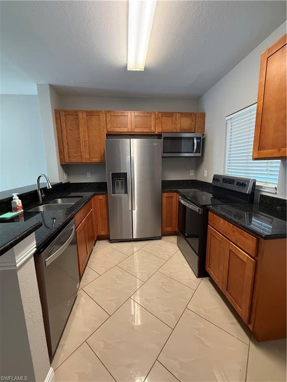 Kitchen featuring appliances with stainless steel finishes, brown cabinets, dark stone countertops, and a textured ceiling