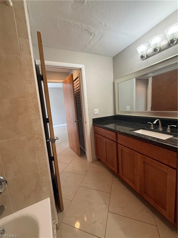 Full bathroom featuring vanity, a textured ceiling, light tile patterned floors, and a textured wall