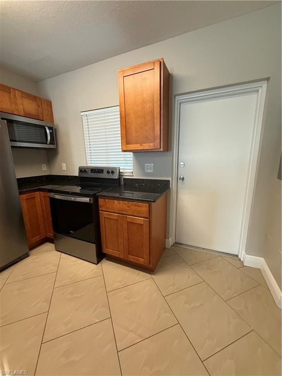 Kitchen with stove, brown cabinetry, refrigerator, dark stone counters, and a textured ceiling