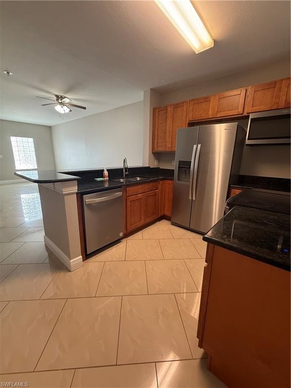 Kitchen featuring brown cabinets, refrigerator, dark stone counters, dishwashing machine, and a ceiling fan