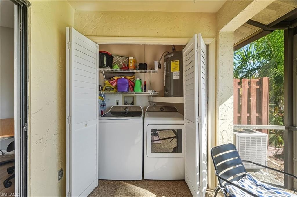 Washroom featuring a textured wall, electric water heater, and washer and clothes dryer