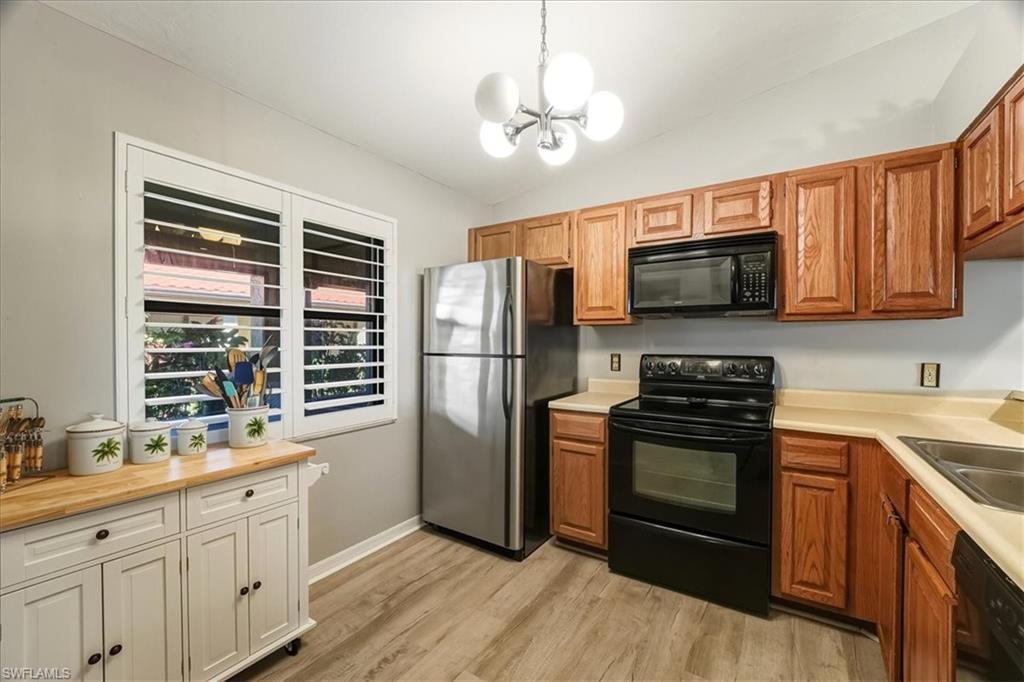 Kitchen featuring black appliances, vaulted ceiling, pendant lighting, light wood-type flooring, and a chandelier