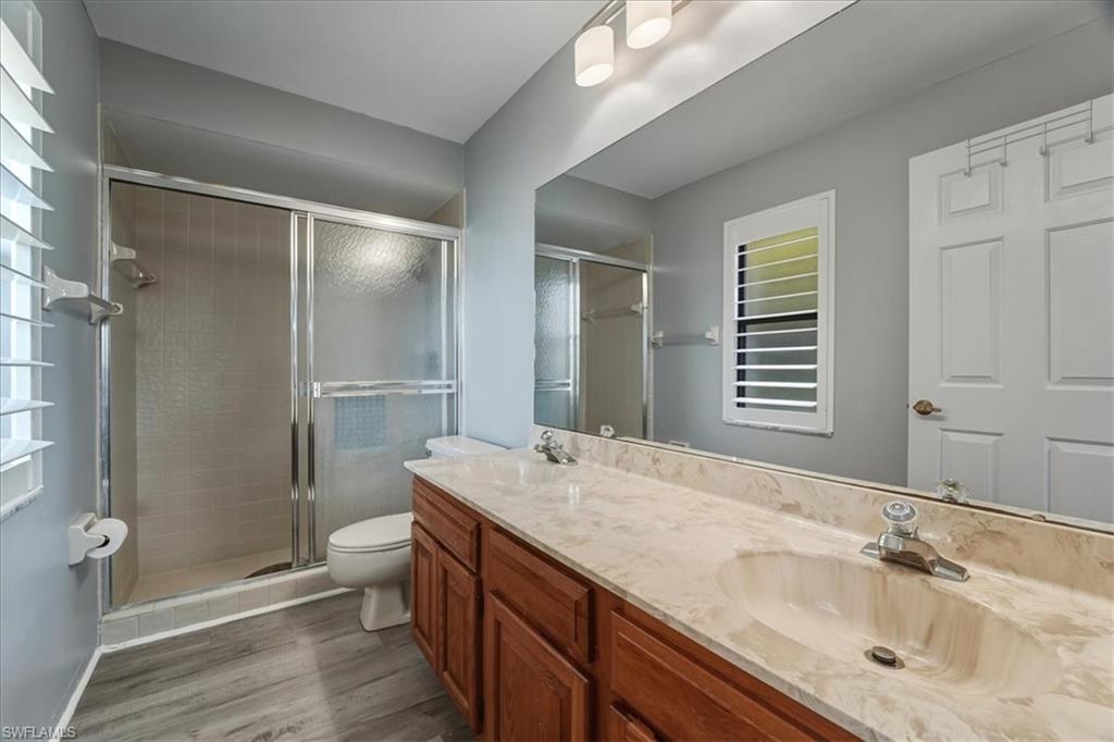 Bathroom with a stall shower, double vanity, and dark wood-style floors
