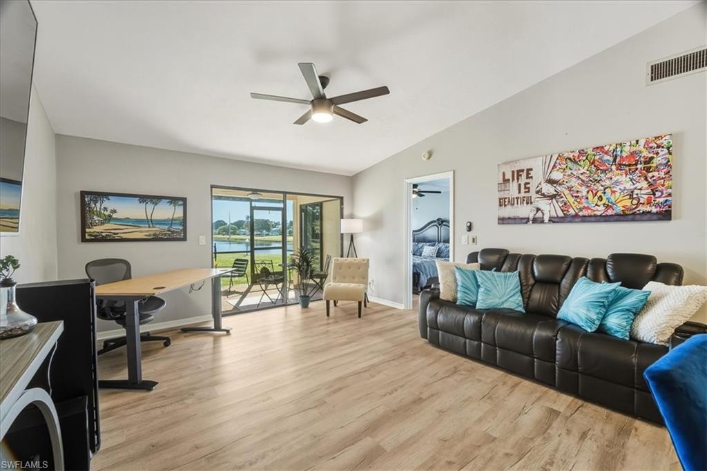 Living area featuring a water view, vaulted ceiling, light wood-style flooring, an office area, and a ceiling fan