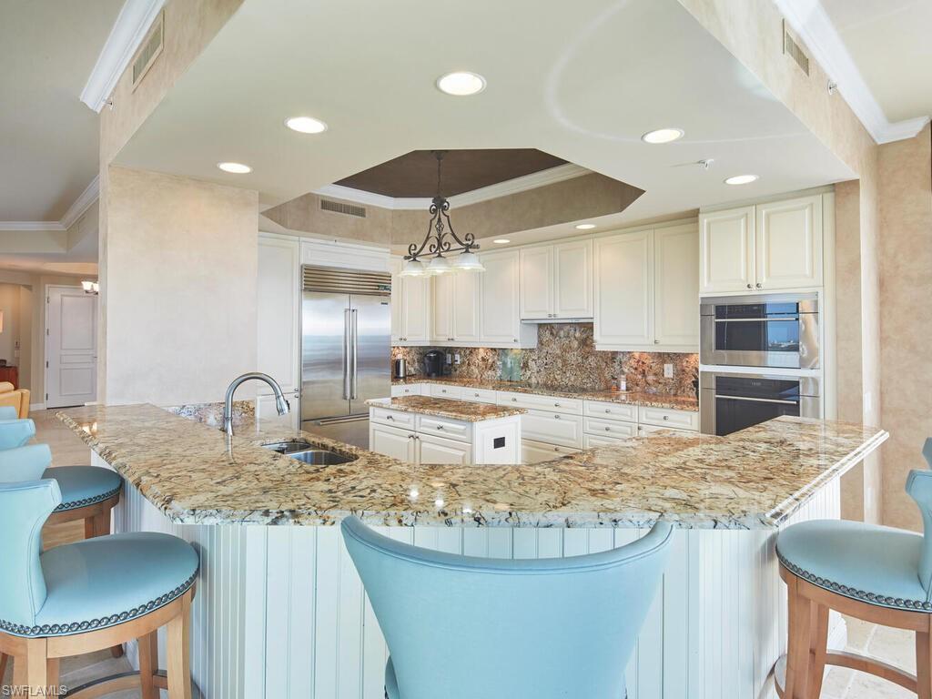 Kitchen featuring ornamental molding, a breakfast bar, a raised ceiling, light stone countertops, and stainless steel appliances