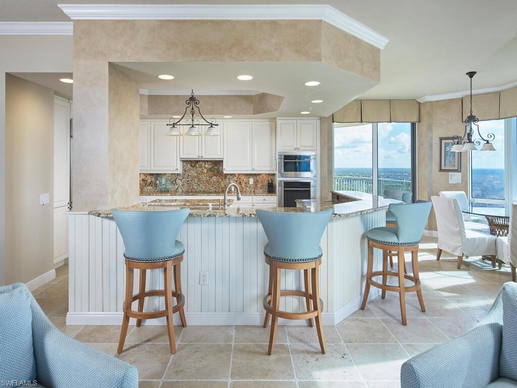 Kitchen with a chandelier, crown molding, light stone countertops, white cabinetry, and backsplash