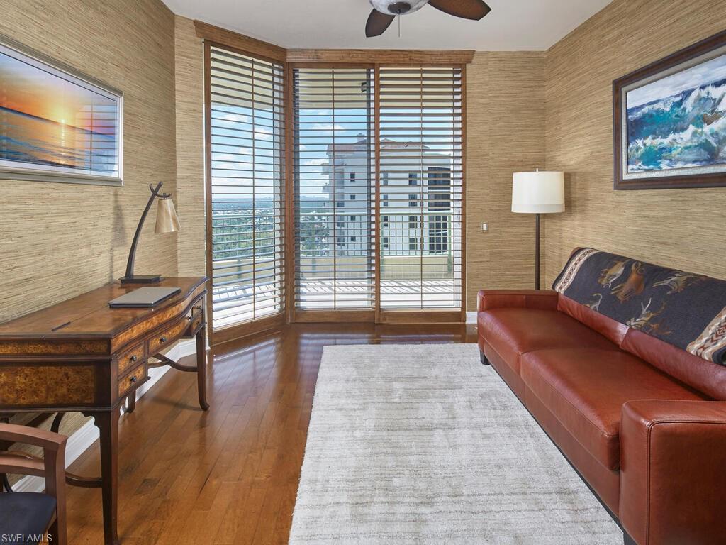 Sitting room with wallpapered walls, ceiling fan, dark wood-type flooring, and an office area