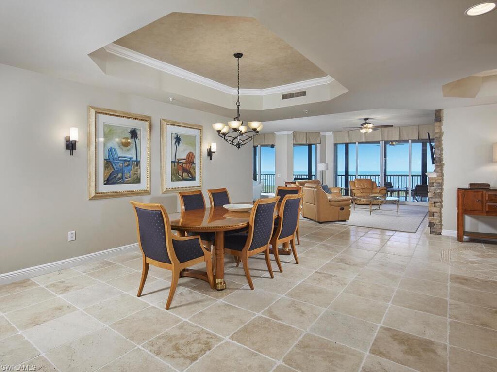 Dining room with crown molding, a chandelier, a tray ceiling, ceiling fan, and light tile patterned floors