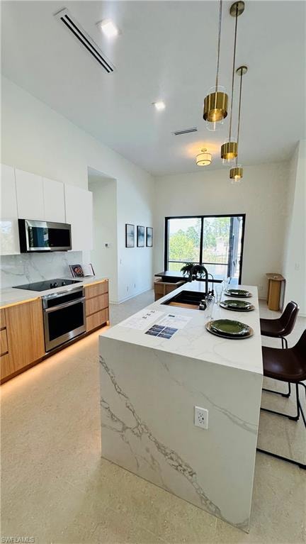 Modern kitchen featuring a waterfall island with stone countertops, a built-in sink with a matte black faucet, integrated stainless steel appliances, and sleek upper cabinetry
