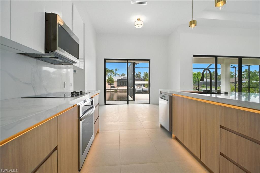 Kitchen featuring modern cabinets, pendant lighting, appliances with stainless steel finishes, and light stone countertops