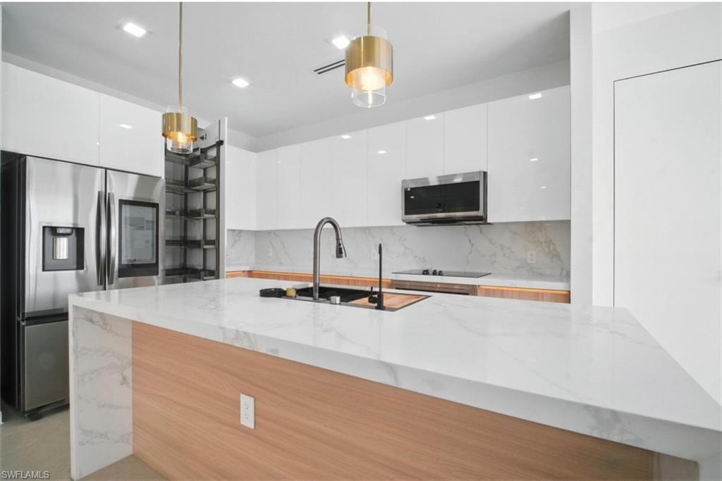 Kitchen with modern cabinets, stainless steel appliances, light stone countertops, backsplash, and dual tone cabinetry