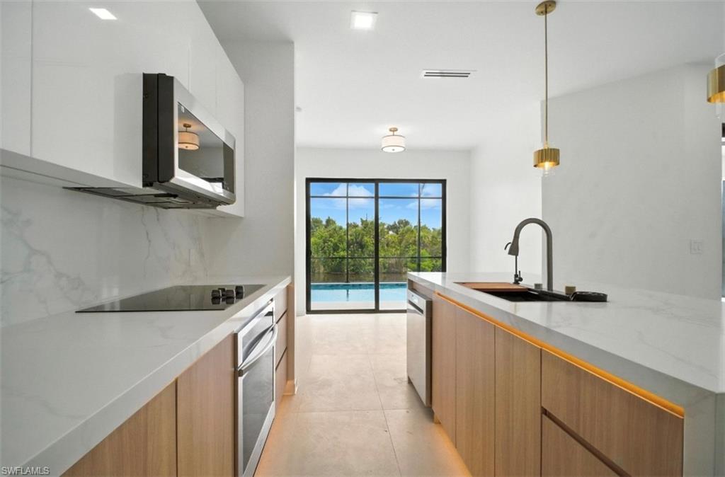 Kitchen with modern cabinets, hanging light fixtures, light stone counters, and stainless steel appliances