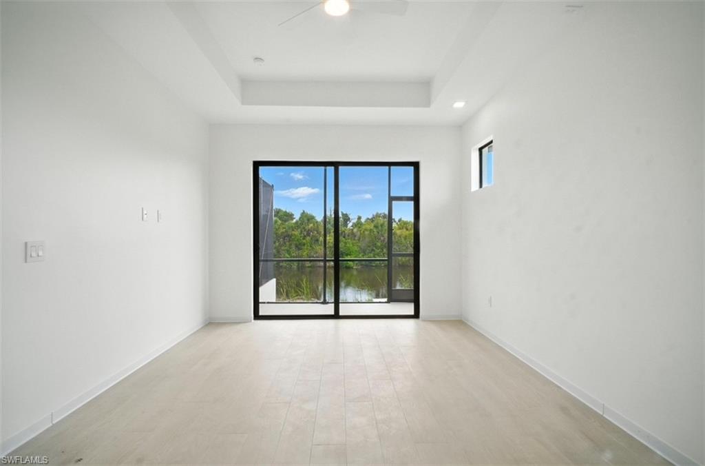 Unfurnished room featuring light wood-style flooring, ceiling fan, a water view, and a raised ceiling