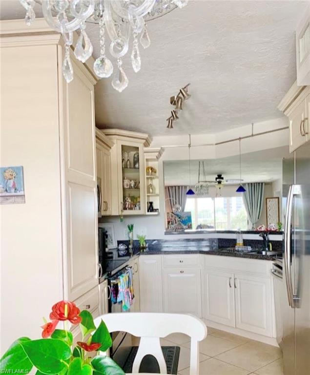 Kitchen with decorative light fixtures, freestanding refrigerator, dark stone countertops, light tile patterned floors, and a textured ceiling