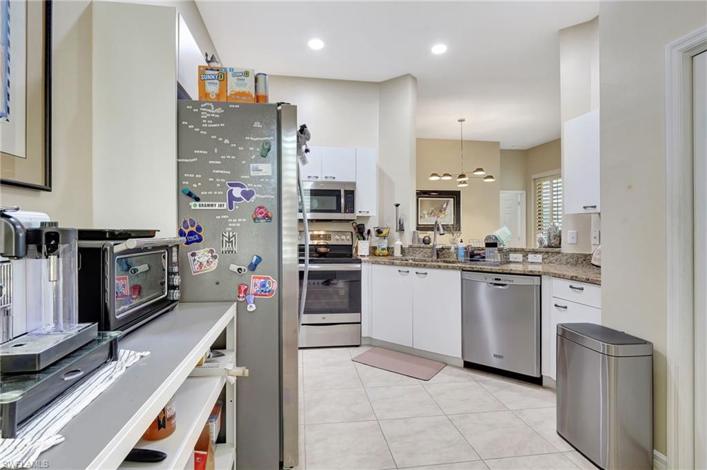 Kitchen featuring light stone countertops, a notable chandelier, white cabinetry, hanging light fixtures, and appliances with stainless steel finishes