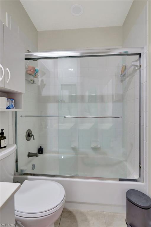 Bathroom with bath / shower combo with glass door, vanity, toilet, and tile patterned flooring