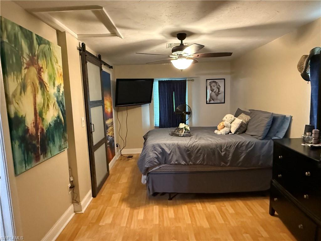 Bedroom with a ceiling fan, light wood finished floors, and a barn door