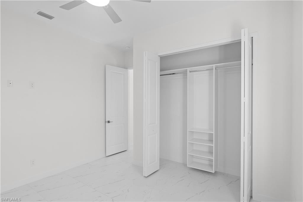 Unfurnished bedroom featuring light marble finish flooring, a ceiling fan, and a closet