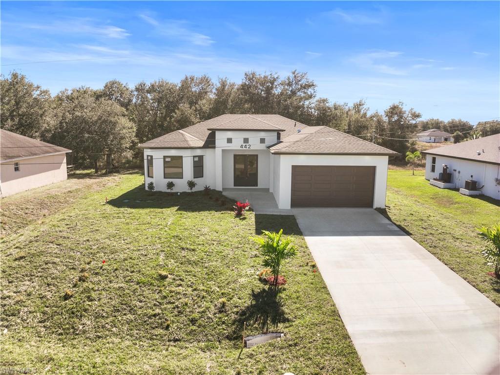 View of front facade with roof with shingles, driveway, stucco siding, and a front yard