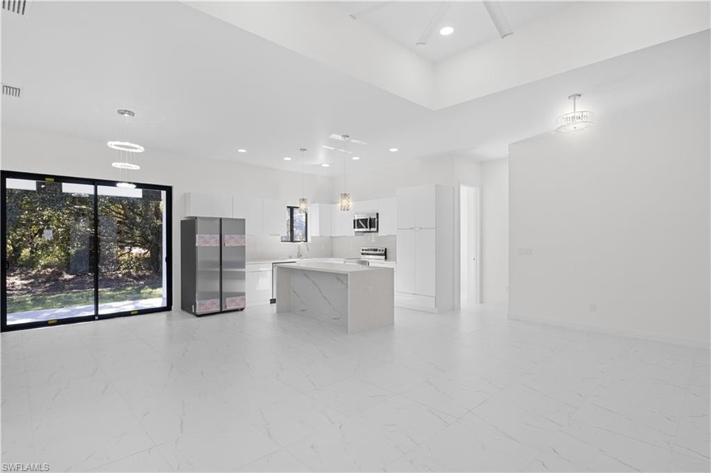 Kitchen featuring decorative light fixtures, white cabinetry, open floor plan, light marble finish flooring, and a kitchen island