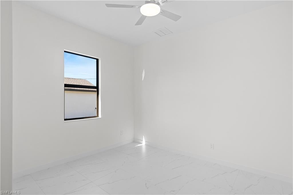 Empty room featuring light marble finish floors and ceiling fan