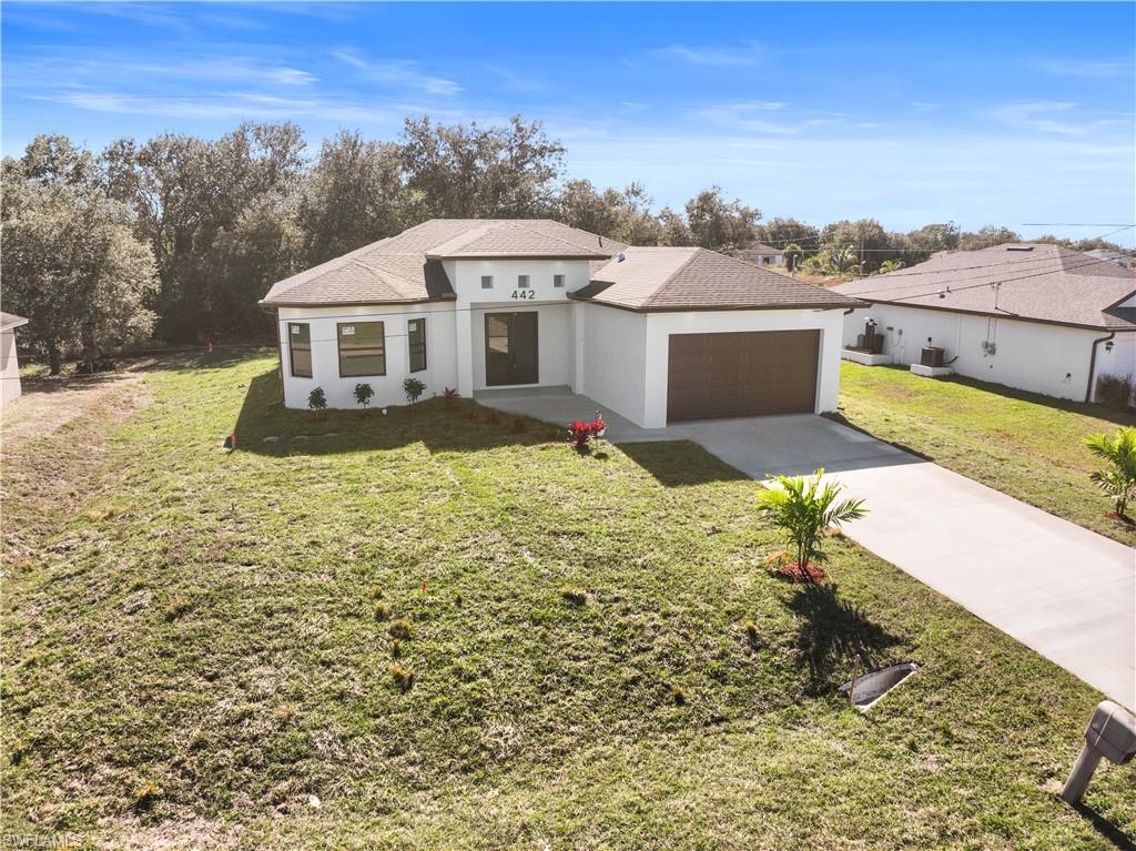 View of front of property with stucco siding, driveway, a front lawn, and roof with shingles