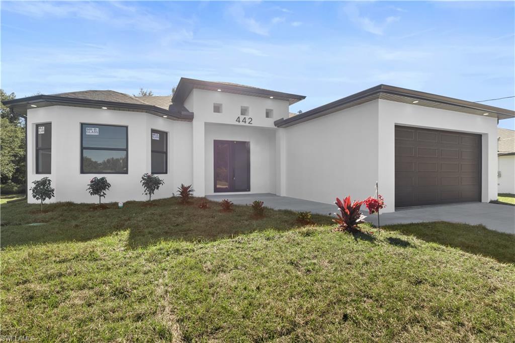 View of front facade featuring an attached garage, a front lawn, stucco siding, and driveway