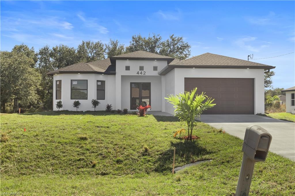 Prairie-style house with concrete driveway, stucco siding, a front lawn, roof with shingles, and an attached garage