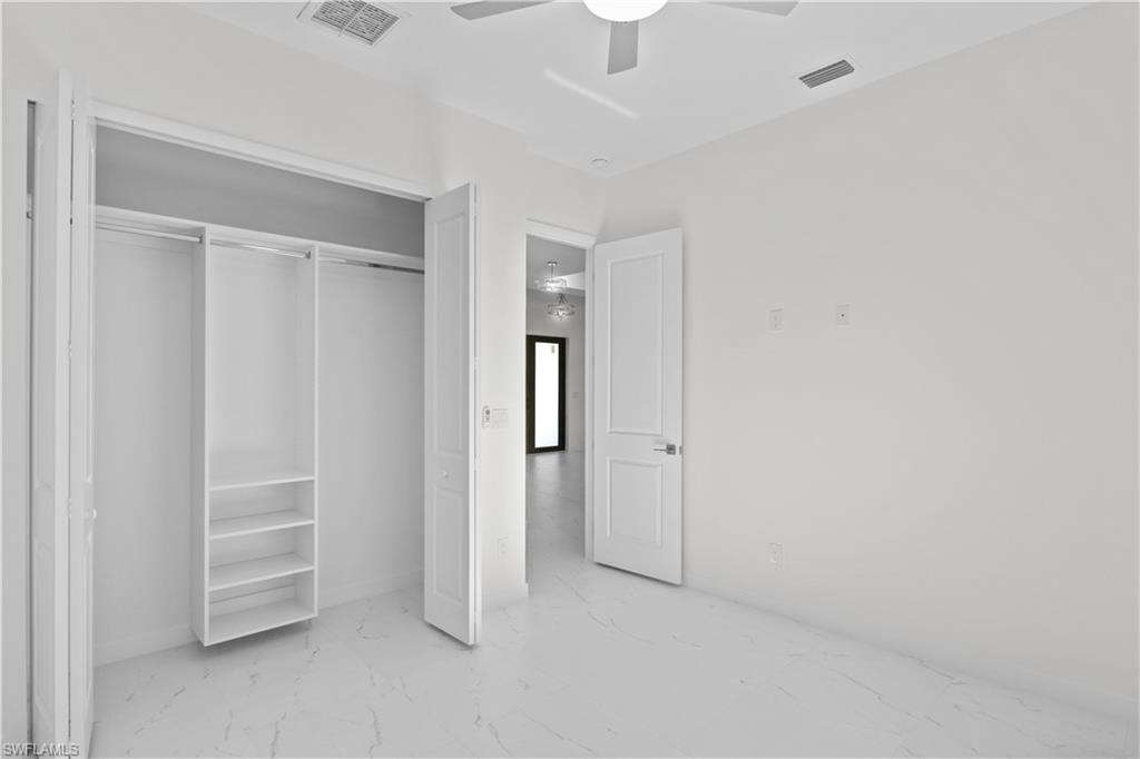 Unfurnished bedroom with light marble finish floors, a ceiling fan, and a closet