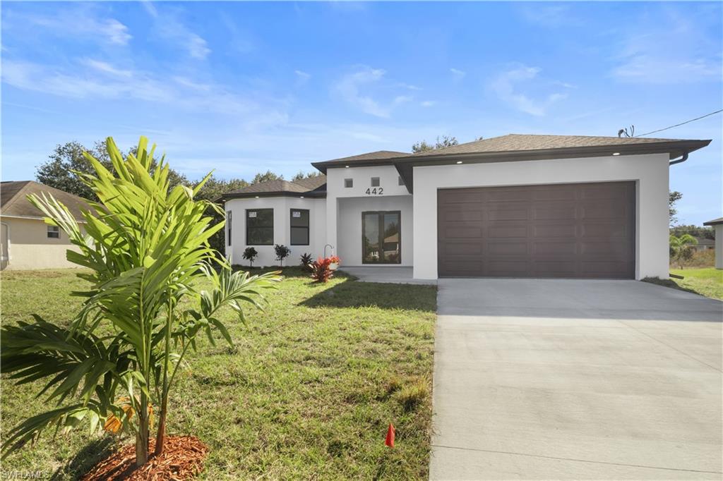 View of front of home featuring driveway, stucco siding, a garage, and a front lawn