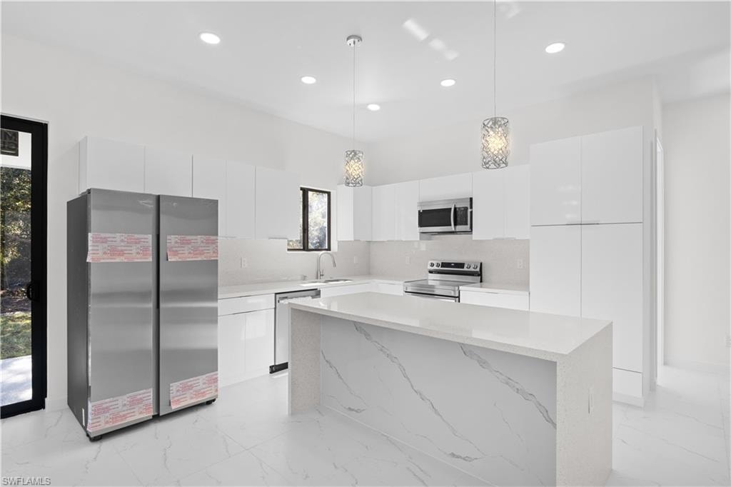 Kitchen featuring modern cabinets, stainless steel appliances, white cabinets, light marble finish floors, and recessed lighting