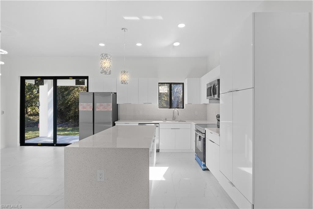 Kitchen with hanging light fixtures, stainless steel appliances, modern cabinets, white cabinets, and recessed lighting